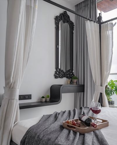 Bedroom vignette with canopy curtains, ornate black mirror, and wine tray on grey blanket