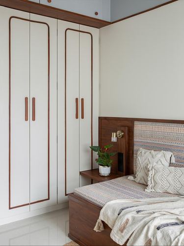 Bedroom corner with white wardrobe with wood-edged doors and a wood-framed patterned headboard