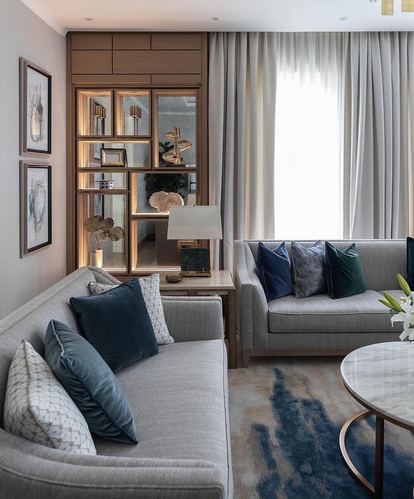 Living room with grey sofas, blue velvet cushions, marble coffee table and lit display cabinet