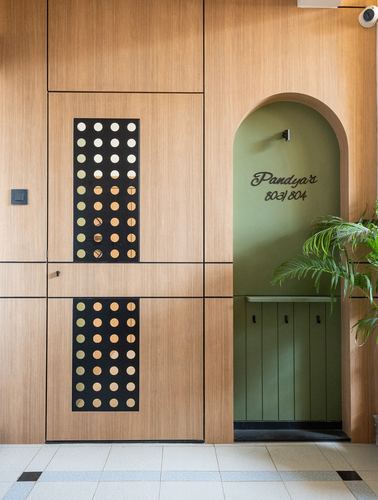 Wooden entryway door with polka-dot inlay panel beside an arched green niche reading Pandya's 803/804