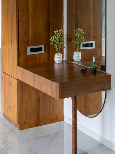 Wooden cantilevered console table with mirror, potted plant, and small objects in a marble-floored foyer