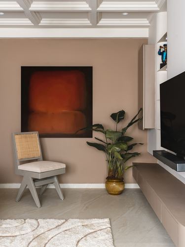 Living room corner with rose wall, abstract orange painting, cane chair, plant, and tv console
