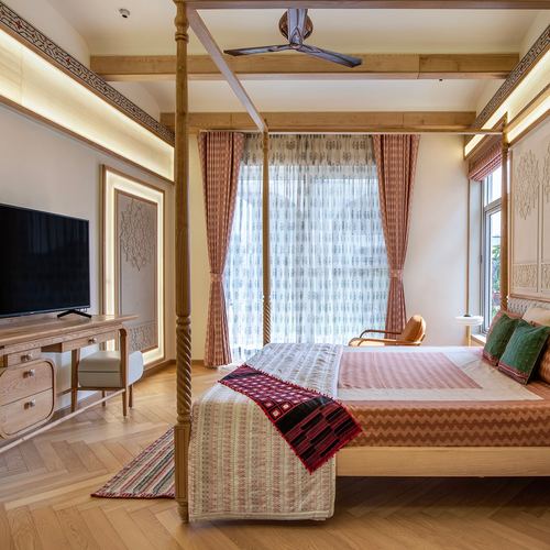 Bedroom with carved wooden four-poster bed, patterned curtains, herringbone wood floor, and wall-mounted tv on desk.