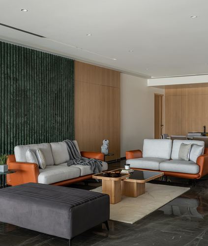 Living room with two grey sofas, orange leather trim, green fluted stone wall, wood coffee table