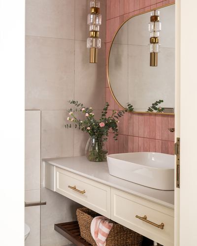 Bathroom vanity with vessel sink, arched brass mirror, pink tiled wall and brass pendant lights