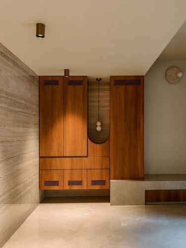 Wooden storage cabinetry with arched niche and pendant light against a travertine wall