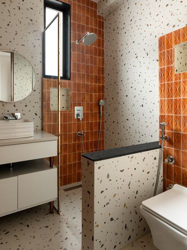 Terrazzo bathroom with orange diamond-tiled shower niche and round mirror above vessel sink