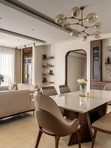 Open-plan dining and living space with fluted wood table, leather chairs, arched mirror, and branching chandelier