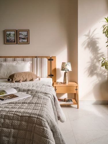 Sunlit bedroom corner with wood headboard, nightstand lamp, and plant shadow on wall