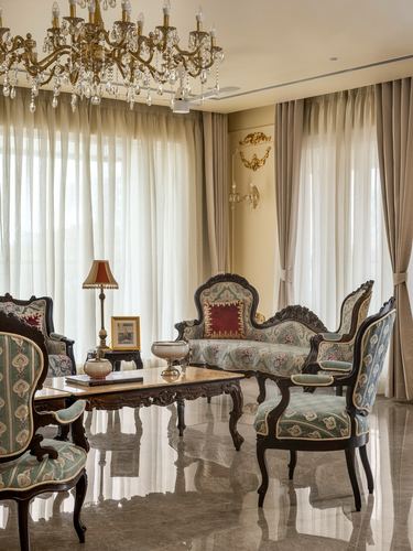 Ornate carved wood sofa and chairs upholstered in teal brocade beneath a crystal chandelier in a marble-floored living room