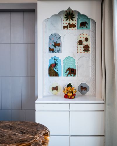 White carved arched pooja niche with painted miniature tiles and small Ganesha idol on cabinet