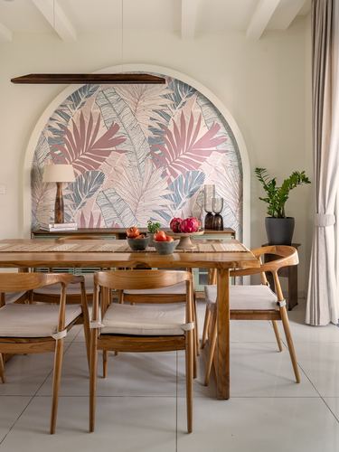 Wooden dining table set before an arched niche with palm-leaf wallpaper