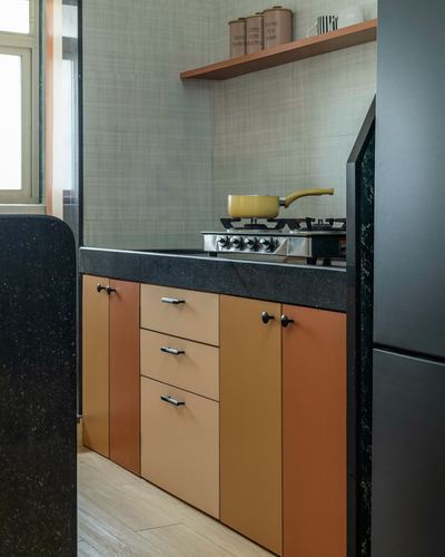 Kitchen corner with terrazzo counter, orange cabinets, gas stove and yellow pot under textured wall shelf