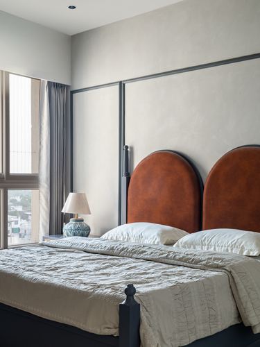 Bedroom with double arched tan leather headboard against panelled wall and daylight window