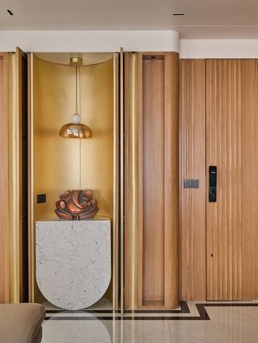 Arched brass niche with pendant light and sculpture beside a fluted wood-panelled entrance door