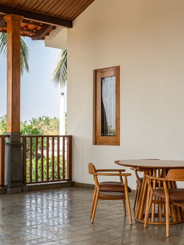 Covered balcony with round wooden dining table, spindle chairs, stone floor, and palm view