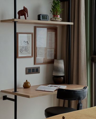 Corner study nook with wooden shelves on black metal frame, framed art, lamp, and black chair