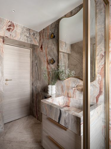 Powder room clad in richly veined stone with brass-framed mirror and floating wood vanity