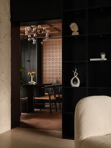View through black shelving into a dining nook with bubble chandelier and terracotta panelled wall