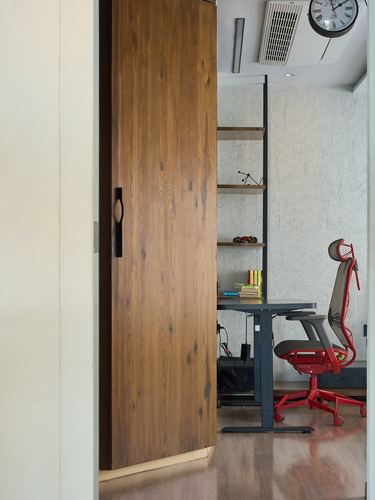 View through a sliding wood door into a home office with textured walls and a red chair