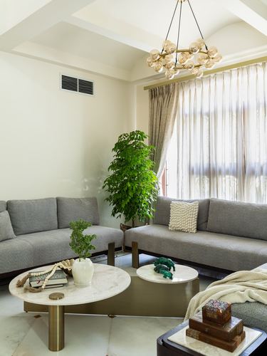 Grey L-shaped sofa around round marble coffee tables under a brass bubble chandelier