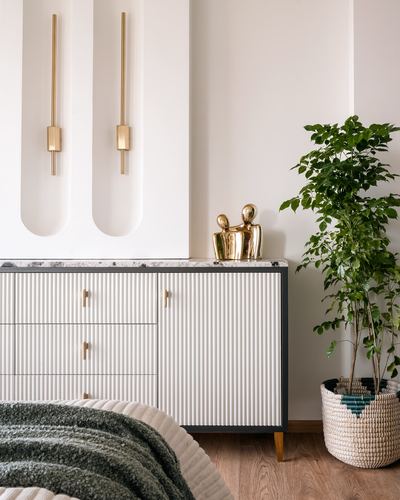 Fluted white sideboard with brass handles beneath arched wall niches and sconces, beside a potted plant