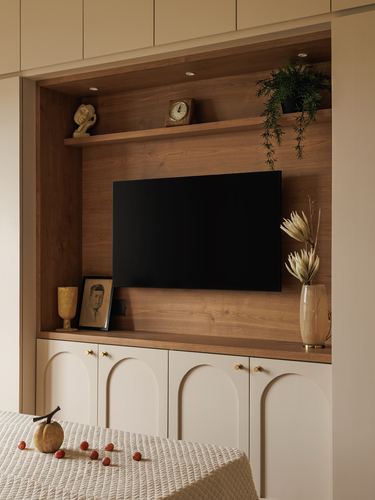 Wall-mounted tv on wood-panelled niche above cream arched cabinetry with brass handles