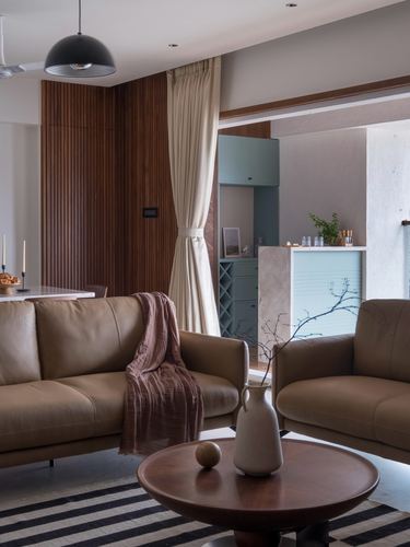 Living room with tan leather sofas, round wood coffee table, and view through curtain to teal kitchen nook