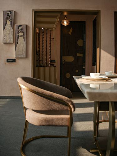 Brass-framed dining chair beside a marble table, with a decorative inlaid door glimpsed through a gilded archway.