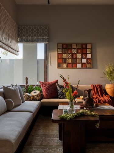 L-shaped beige sofa with patterned cushions beside a wooden coffee table and patchwork wall art