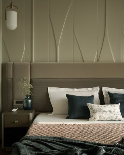 Bedroom with sculpted panelled wall, taupe upholstered headboard, and dark green cushions