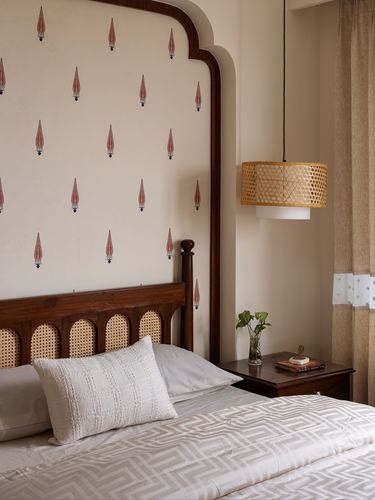 Bed with cane headboard against block-print wallpaper, rattan pendant light beside curtained window