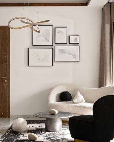 Living room corner with framed art gallery wall, curved boucle sofa, round marble coffee table, and ribbon pendant light