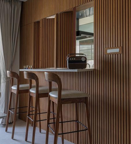Three wooden bar stools at a stone counter beneath a fluted wood-clad pass-through window into a kitchen