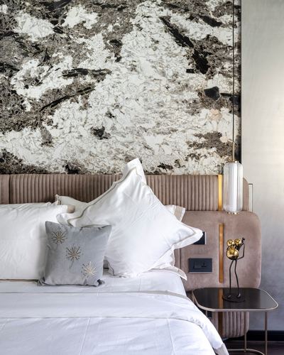 Bedroom with tufted blush headboard against a dramatic black-and-white stone wall and brass bedside lamp