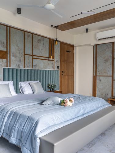 Bedroom with veined stone-panel wall, teal ribbed headboard, pale blue bedding and hanging pendant lights