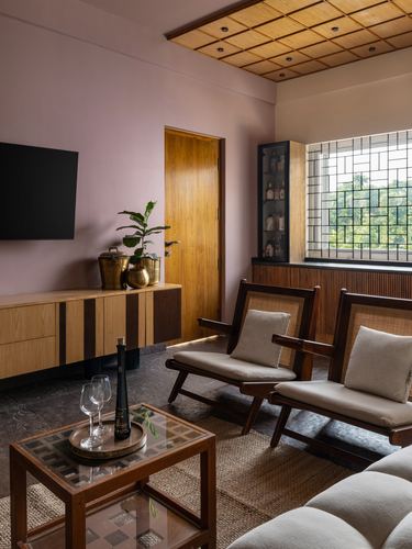 Living room with pink walls, cane lounge chairs, wooden sideboard and slatted ceiling detail