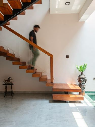 Man descending a wooden and glass staircase into a marble-floored foyer with an urn and plant