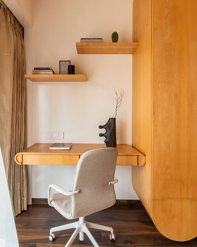 Wall-mounted wooden desk and shelves in a small study nook with a curved wardrobe