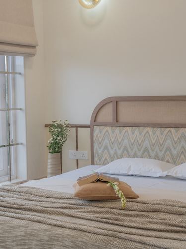 Bedroom with arched upholstered headboard, white linens, vase of flowers by grilled window