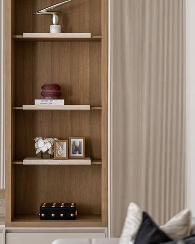 Wood-lined open shelves styled with sculpture, books and frames beside a fluted taupe wall