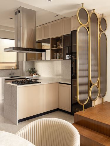 Beige kitchen with stone counters beside a gold ribbed-glass oval screen and wooden stairs