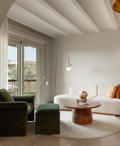 Living room with boucle sofa, green velvet armchair, round wood table, vaulted ceiling and balcony view