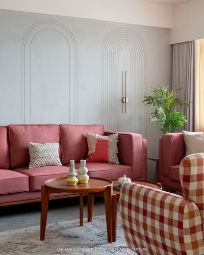 Pink velvet sofa against grey arched-moulding wall with wooden coffee tables and checkered armchair