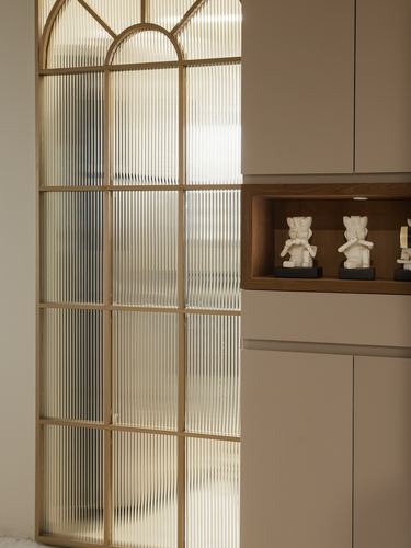 Arched fluted glass door with brass frame beside a lit wooden display niche holding figurines