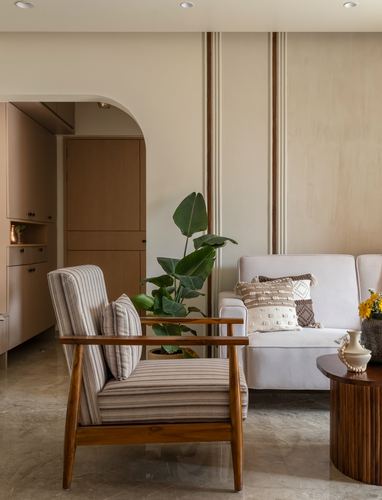 Living room with striped armchair, white sofa, plant, and arched doorway to kitchen