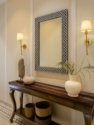 Foyer with inlay mirror, brass sconces, wooden console table and patterned floor tile
