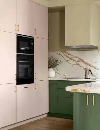 Corner kitchen with blush pink tall cabinets, green base units, marble-look backsplash and brass handles