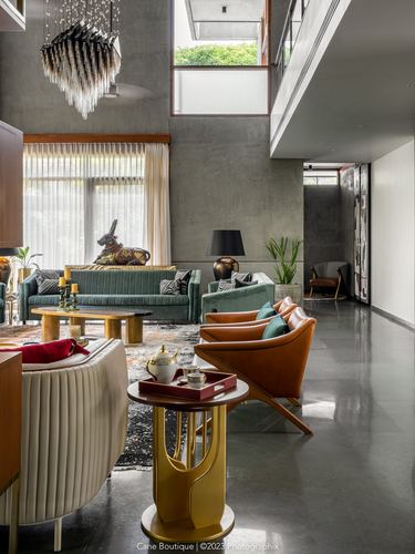 Double-height living room with orange leather chairs, green sofa, brass table and concrete wall