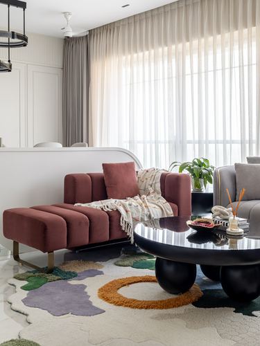 Living room corner with maroon velvet chaise, black round coffee table, and multicolor tufted rug
